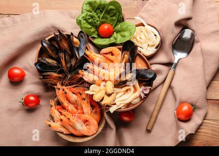 Schüssel mit leckerer Cacciucco-Suppe und Zutaten auf Holzboden Stockfoto