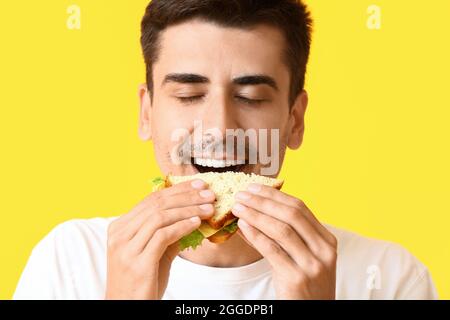 Junger Mann, der leckeres Sandwich auf farbigem Hintergrund isst Stockfoto