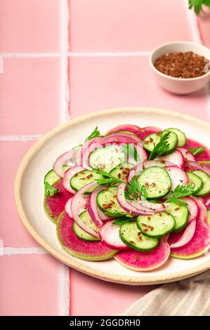 Gesunder veganer Salat mit Wassermelonen-Rettich, Gurke und roter Zwiebel auf rosa Fliesenhintergrund. Stockfoto