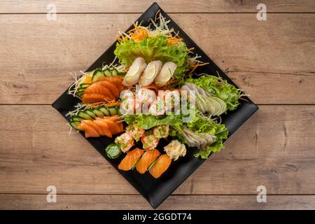 Mix aus Sushi und Niguiris auf schwarzem Teller auf Holztisch Stockfoto