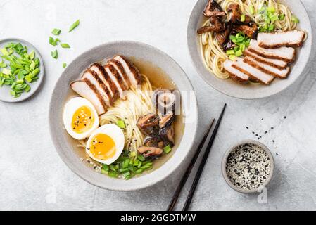 Ramen-Schüssel mit Schweinefleisch und Ei auf grauem Beton-Tischhintergrund, Draufsicht Stockfoto