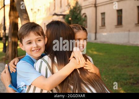 Mutter sagt ihren kleinen Kindern in der Nähe der Schule Auf Wiedersehen Stockfoto