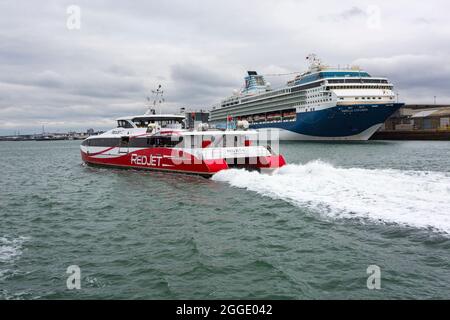 Der Red Jet 6 fährt nach Southampton, vorbei an dem TUI Marella Explorer-Schiff, das im August an den Docks von Southampton, Hampshire, Großbritannien, festgemacht wurde Stockfoto