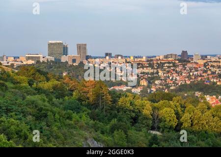 Prag, Tschechische Republik - August 21 2021: Blick auf die Stadt aus der Ferne mit Gebäuden und einem Wolkenkratzer. Grüne Bäume im Vordergrund. Sonniger Sommer Stockfoto