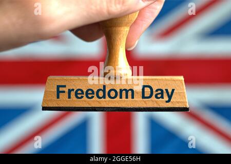Deutschland. Juli 2021. Ein symbolischer Holzstempel mit der Aufschrift 'Freedom Day', der von einer Hand vor einer verschwommenen Flagge Großbritanniens (GB) gehalten wird, im Hintergrund der 'Union Jack'. Großbritannien hob am 19. Juli 2021 trotz hoher und steigender Inzidenzwerte alle Corona-Maßnahmen und -Beschränkungen für den „Freedom Day“ auf. Foto mit Komposition [M]. | Model Released Credit: dpa/Alamy Live News Stockfoto