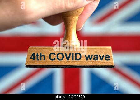 Deutschland. Juli 2021. Ein symbolischer Holzstempel mit der Aufschrift '4th COVID Wave', der von einer Hand vor einer verschwommenen Flagge Großbritanniens (GB) gehalten wird, im Hintergrund der 'Union Jack'. Großbritannien hob am 19. Juli 2021 trotz hoher und steigender Inzidenzwerte alle Corona-Maßnahmen und -Beschränkungen für den „Freedom Day“ auf. Foto mit Komposition [M]. | Model Released Credit: dpa/Alamy Live News Stockfoto