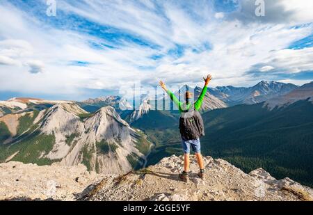 Wanderer streckt seine Arme in die Luft, Berglandschaft mit Flusstal und Gipfeln, Gipfel mit orangen Schwefelablagerungen, Umstürzen Berg, Panorama Stockfoto