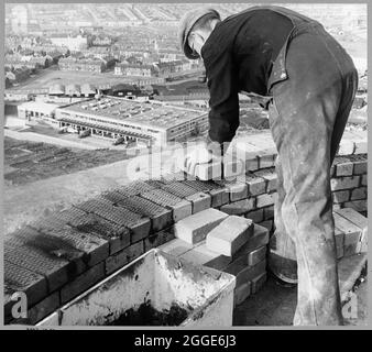 Ein Arbeiter, der während des Baus des Kraftwerks Plymouth 'B' Ziegelsteine an die Oberseite des Schornsteinschachts legte. Dieses Bild wurde als Teil des Breaking New Ground Project in Zusammenarbeit mit dem John Laing Charitable Trust in den Jahren 2019-20 katalogisiert. Stockfoto