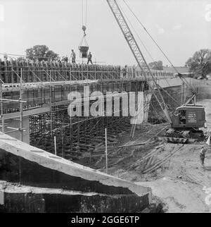 Ein Blick auf den Bau der Autobahn Birmingham nach Preston (M6), der das Betonieren der großen nachgespannten Balken auf der Brücke 306 (Barn Bank Lane Bridge) vor Ort zeigt, wobei ein Kran einen Betontrichter absenkt und das Team, das an der Brücke arbeitet, an der Brücke beteiligt ist. Diese Straßenbrücke, die sich an der SJ9211419999 befindet, wurde im März 1962 eröffnet. Das Foto wurde im September 1961 in Laings monatlichem Newsletter „Team Spirit“ veröffentlicht. Stockfoto