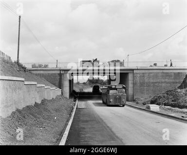 Ein Blick auf den Bau der Autobahn Birmingham nach Preston (M6), der einen Midland Red Bus (Service 98 nach Coppenhal) zeigt, der unter der Burton Manor Road Bridge fährt, wobei die Bauarbeiten auf der Autobahn darüber stattfinden. Die Position dieser Straßenbrücke befindet sich an der Netzreferenz SJ9155420677. Stockfoto