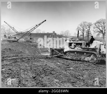 Ein Blick auf den Bau der Stafford-Umgehungsstraße auf der Birmingham to Preston Motorway (M6), mit Blick nach Norden über Rising Brook in Richtung Highfields Farm Access Bridge und zeigt Laing-Bagger und einen Bulldozer, der Torfentfernung durchführt. In dem Album heißt es in der getippten Beschriftung unter dem Foto: „Blick nach Norden über Rising Brook, wo vor dem Bau des Autobahndamms eine große Torf-Tasche (50,000 Kubikmeter) entfernt und durch eine Tonrückfüllung ersetzt wird. Im Hintergrund ist die Zugangsbrücke zur Highfields Farm zu sehen, die praktisch vollständig ist.“ Die Arbeiten an der Stafford-Bypass-Station begannen Stockfoto