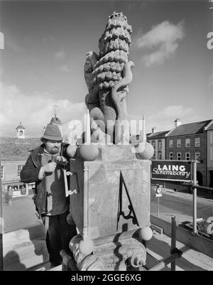 Ein Laing-Steinmetzer, der Reparaturen an der Spitze des Marktkreuzes in Carlisle durchführt, mit einem Laing-Steinmetzschild im Hintergrund. Die Laing-Steinmetzerei war ein kleiner Spezialbereich der Laing-Unternehmensgruppe mit Sitz in den Büros in der Dalston Road, Carlisle. Die erbrachten Leistungen umfassten Voruntersuchungen, Standortuntersuchungen, Steinmetzbau, Restaurierung, Reparatur, Mauerbau, Reinigung, Wandung und Verkleidung. Stockfoto