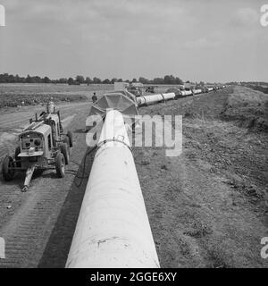 Eine Ansicht der Fens-Gaspipeline mit schützenden Vordächern an den Fugen entlang des Rohres, an denen Unterschweißen durchgeführt wurden. Die Arbeiten zur Verlegung der Fens-Gaspipeline begannen im Juni 1967 und waren ein Joint Venture zwischen Laing Civil Engineering und den französischen Unternehmen Entrepose und Grands Travaux de Marseille (GTM) für den Gasrat. Über 600 Männer arbeiteten an dem Projekt, Stahlrohre mit einem Durchmesser von 36 Zoll zu verlegen, beginnend bei West Winch in Norfolk, wo es mit dem nächsten Vertrag in Woodcroft Castle in Cambridgeshire in Verbindung gebracht wurde. Die Pipeline überquerte vier Flüsse und zahlreiche Deiche und Gräben. Stockfoto