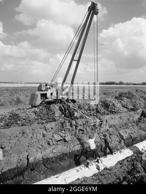 Eine Rohrleitung mit einem Seitenausleger und ein Team von Arbeitern, die einen Abschnitt der Fens-Gaspipeline in einen Graben verlegen. Die Arbeiten zur Verlegung der Fens-Gaspipeline begannen im Juni 1967 und waren ein Joint Venture zwischen Laing Civil Engineering und den französischen Unternehmen Entrepose und Grands Travaux de Marseille (GTM) für den Gasrat. Über 600 Männer arbeiteten an dem Projekt, Stahlrohre mit einem Durchmesser von 36 Zoll zu verlegen, beginnend bei West Winch in Norfolk, wo es mit dem nächsten Vertrag in Woodcroft Castle in Cambridgeshire in Verbindung gebracht wurde. Die Pipeline überquerte vier Flüsse und zahlreiche Deiche und Gräben. Stockfoto