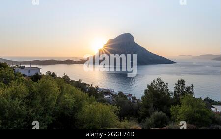 Sonnenschein über Meer und Hügeln in Abendstimmung, Dorfblick auf Mirties und Masouri, links Telendos Island, Kalymnos, Dodekanes, Griechenland Stockfoto