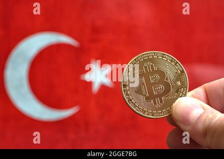 Eine Bitcoin-Münze, die von einer Hand vor einer Darstellung der türkischen Flagge gehalten wird. Die Türkei versus Kryptowährung und verbietet alle Zahlungen mit digitalen Währungen. Stockfoto