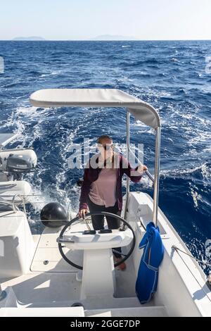 Junge Frau am Steuer im Cockpit auf dem Deck eines Segel-Katamarans, Segeltörn, Dodekanes, Griechenland Stockfoto