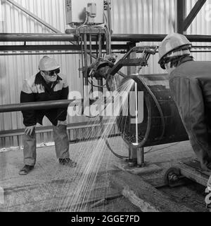 Zwei Laing-Arbeiter bei Greythorp beobachten ein Präzisionswerkzeug, das durch ein großes Metallrohr schneidet. In den frühen 1970er Jahren bauten Laing Pipelines Offshore die Graythorp-Fabrikationswerft und das Trockendock auf dem Gelände der alten William Gray Shipyard. Das Unternehmen schuf ein Trockendock, das für den Bau von Bohrgeräten mit fester Plattform in der Nordsee für das Nordseeölprojekt BP verwendet wurde. Bis 1972 arbeiteten eintausend Mann vor Ort, um eine Rohrstruktur zu bauen, die ein Bohrgerät in der Nordsee für das Forties Oilfield unterstützen würde. Stockfoto