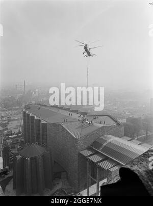 Ein Blick über die Coventry Cathedral vom Turm der alten Kathedrale, der einen RAF Belvedere Hubschrauber zeigt, der den 80 Fuß langen Bronzeturm auf das Dach senkt. Das Foto wurde während der „Operation Rich man“ aufgenommen, einem gemeinsamen Projekt, an dem Mitarbeiter der Royal Air Force und Mitarbeiter von Laing beteiligt waren. Dazu wurde ein RAF Belvedere Hubschrauber hochgezogen, um den 80 Fuß großen Bronzeturm auf der neuen Kathedrale zu platzieren. Der Teil der Operation zur Senkung des 1/2 Tonnen schweren Kreuzes, das auf dem Turm sitzt, musste aufgrund windiger Bedingungen verschoben werden. Stockfoto