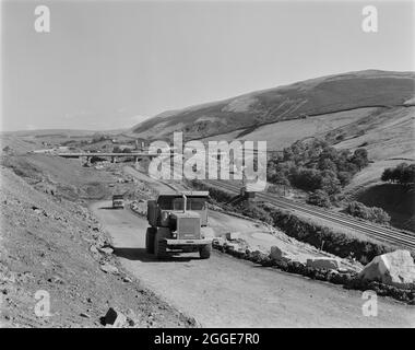 Ein Blick auf den Bau der Autobahn M6 durch die Lune Gorge, mit Muldenkipper auf der Haul Road, die vom Viadukt des Lawtland House und der Roger Howe Brücke führt. Die Arbeiten am Abschnitt Lune Gorge der Autobahn M6 zwischen Killington und Tebay (Junction 37 - Junction 38) wurden von John Laing Construction Ltd. Durchgeführt. Die Arbeiten begannen im Oktober 1967 und die Autobahn wurde im Oktober 1970 für den Verkehr geöffnet. Auf diesem Abschnitt der M6 wurden 20 Brücken und 17 Sekten über Flüsse und Bäche gebaut. Das Lawtland House Viadukt (NY6116502666) wurde gebaut, um die A685 über die M6 und den Roge zu transportieren Stockfoto