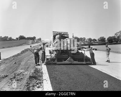 Ein Blick auf die Arbeiter von Laing, die eine Fertiger-Maschine bedienen und einen asphaltierten Grundkurs zur Straße von London nach Yorkshire Motorway (M1) legen. Dieses Bild wurde als Teil des Breaking New Ground Project in Zusammenarbeit mit dem John Laing Charitable Trust in den Jahren 2019-20 katalogisiert. Stockfoto