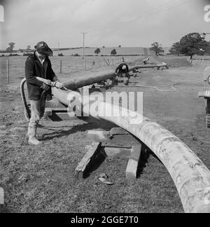 Ein Arbeiter, der auf der Ölpipeline von Mersey Schüsse (Betonspritzen) ausführt, bereit für eine Flussüberquerung. Die Mersey-Ölpipeline wurde 1967 von Laing Civil Engineering in Zusammenarbeit mit den französischen Unternehmen Entrepose und Grands Trevaux de Marseille (GTM) installiert. Es ist 88 Meilen lang und verläuft vom Ellesmere Port zum Kingsbury Oil Terminal, das die Midlands bedient. Die Pipeline musste viermal den Fluss Trent überqueren, auch den Fluss Tame und eine Reihe von Bächen und Kanälen. Das abgebildete Foto wurde im November 1967 im Laing-Newsletter „Team Spirit“ veröffentlicht. Stockfoto