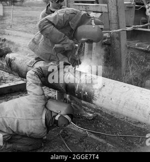 Zwei Schweißer bei der Arbeit an der Mersey-Ölpipeline. Die Mersey-Ölpipeline wurde 1967 von Laing Civil Engineering in Zusammenarbeit mit den französischen Unternehmen Entrepose und Grands Trevaux de Marseille (GTM) installiert. Es ist 88 Meilen lang und verläuft vom Ellesmere Port zum Kingsbury Oil Terminal, das die Midlands bedient. Stockfoto