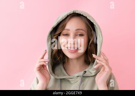 Glückliche Zähne Lächeln Frau hält Kapuze mit seinen Händen kaukasische Frau genießen gekleidet Oversize Hoodie rosa Hintergrund Nahaufnahme Porträt Stockfoto