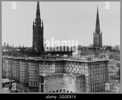 Ein Blick aus dem Nordosten zeigt die Nord- und Ostmauern der Coventry Kathedrale während des Baus, mit der alten Kathedrale und der Holy Trinity Church im Hintergrund. Nach dem Bombenangriff auf die Kathedrale von Coventry im November 1940 wurde 1950 ein Wettbewerb gestartet, um einen Entwurf für eine neue Kathedrale zu finden. Das Siegerdesign stammt von Sir Basil Spence (1907-1976) aus einem von über 200 eingereichten Designs. Die Bauarbeiten fanden zwischen Mitte der 1950er und 1962 statt. Am 23. März 1956 legte Königin Elisabeth II. Den Grundstein. Stockfoto