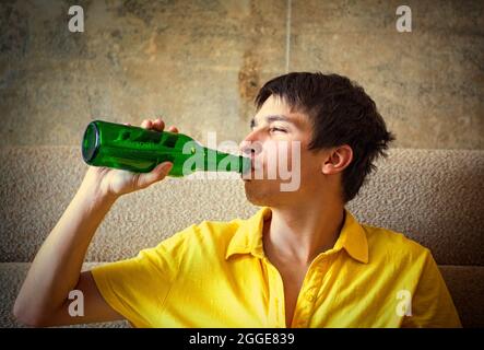 Vignettierung Foto des jungen Mannes Trinken Sie ein Bier auf dem Sofa im Haus Stockfoto