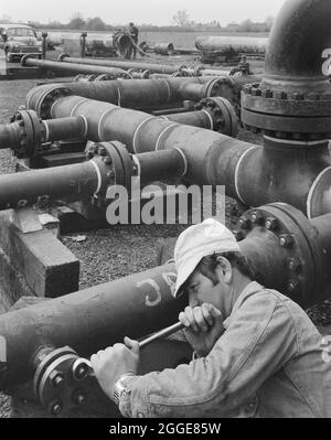 Ein Arbeiter, der Schrauben an einem komplexen Rohrstück im Vorertragslager von Bottesford festzieht. Im Jahr 1969 gründeten Laing Pipelines ihr Pre-Yield-Depot auf dem Bottesford Airfield in der Nähe von Grantham. Stahlrohre mit großem Durchmesser für Gasversorgungsleitungen konnten im Depot auf ihre Ausbeute unter Hydraulikdruck getestet werden, und es gab auch eine große Wellblech-Fertigungshalle. Stockfoto