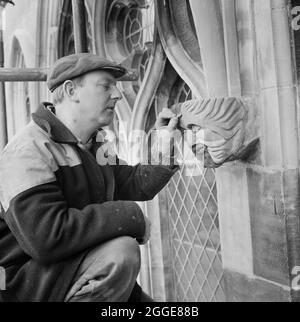 Der Steinmetzmeister Ted Drinkwater, der in der Kathedrale von Carlisle arbeitete, überprüfte einen Steinkopf auf der Nordwand der Kathedrale. Die Hälfte der Oberfläche wurde mit SBD Certite als Klebstoff ersetzt. Dieses Foto ist Teil einer Charge, die von Laing aufgenommen wurde, um Restaurierungsarbeiten zu zeigen, die mit SBD Certite durchgeführt werden. 1961 begann N M Phillips, der Architekt der Kathedrale von Carlisle, bei der Restaurierung der Kathedrale mit dem Bindematerial SBD Certite zu experimentieren. Es wurde an allen, bis auf eines der dekorierten gotischen Fenster des Südlichen Klerestorius, verwendet und als dieses Foto aufgenommen wurde, war es U Stockfoto