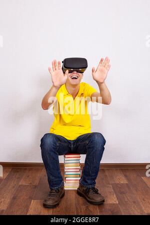 Glücklicher junger Mann in Virtual Reality Headset auf dem Boden mit Büchern Stockfoto