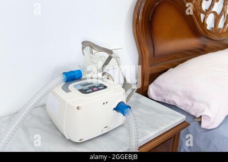 CPAP-Gerät mit Luftschlauch und Kopfmaske auf Nachttisch Stockfoto