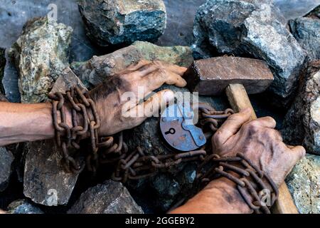 Sklave harte Arbeit. Harte Arbeit. Die Hände des Sträflings halten einen Hammer. Wunsch, frei zu sein. Der Wunsch, die Fesseln zu brechen Stockfoto