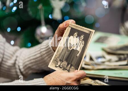 Alte Frau hält und altes Foto auf Weihnachtsbaum Hintergrund. Familie und Leben Werte Konzept. Stockfoto