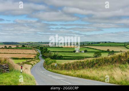 Eine lange, kurvenreiche Asphaltstraße durch einige der schönsten, gut gepflegten ländlichen Ackerflächen in Cornwall, England, mit einem Flickenteppich aus bunten Feldern. Stockfoto