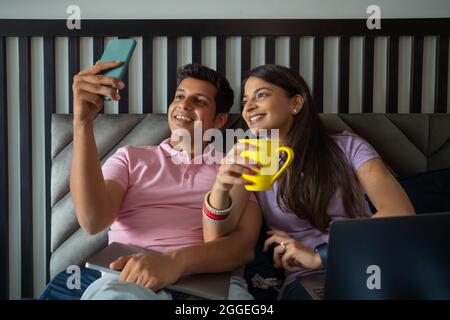 Das junge Brautpaar klickt auf ein Selfie, während die Frau in ihrem Schlafzimmer Kaffee trinkt. Stockfoto