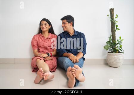 Junge Brautpaar, die in der Wohnung sitzen, mit Ehemann, der Frau liebenswert ansieht. Stockfoto