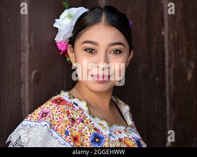 Junge schöne mexikanische Frau mit Make-up trägt traditionelles Maya Yucatecan folklorisches Kleid mit Blumen im Haar und posiert für die Kamera. Stockfoto