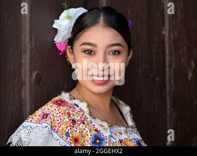 Junge schöne mexikanische Frau mit Make-up trägt traditionelles Maya Yucatecan folklorisches Kleid mit Blumen im Haar und lächelt für den Betrachter. Stockfoto