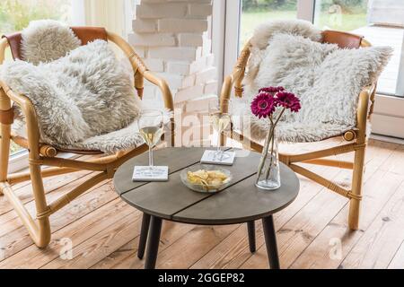 Zwei Korbsessel mit Kissen und ein Couchtisch mit Weingläsern sowie ein Snack im Wintergarten Stockfoto