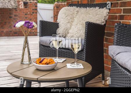 Rattanstuhl mit Kissen und einem kleinen Tisch mit Weingläsern auf einer Holzterrasse, Steinwand im Hintergrund Stockfoto