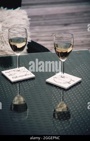 Zwei Gläser Wein mit Spiegelung auf dem gläsernen Gartentisch, vertikal Stockfoto