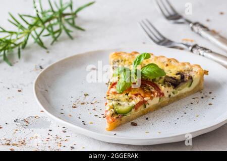 Stück Gemüsetorte mit Pilzen, Tomaten und Zucchini auf weißem Hintergrund Stockfoto