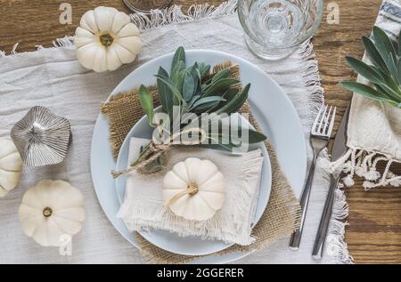 Stellen Sie das Setting auf einen Holztisch mit weißen Mini-Kürbissen, Salbeiblättern und Kristallgläsern, dekoriert für Thanksgiving Day oder Halloween, Draufsicht. Stockfoto