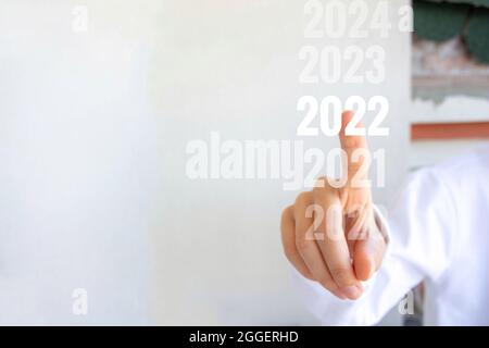 Junge Frau zeigt auf die Jahre. Konzept für das neue Jahr 2022. Stockfoto