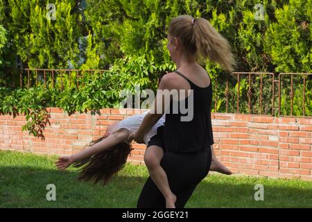 Die junge Frau tanzt im Garten mit ihrer kleinen Tochter in den Armen. Selektiver Fokus. Film. Stockfoto