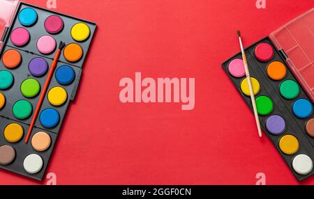 Bunte Farben und Pinsel auf rotem Hintergrund, leerer Raum, Schablone. Kreative Kinder, malen und zeichnen. Bildung, Back to School Konzept. Stockfoto
