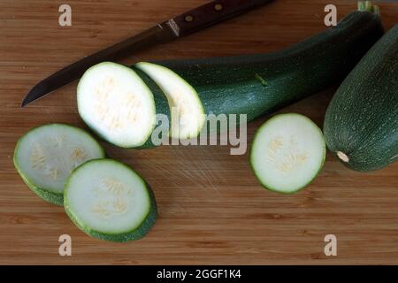 Reife rohe runde Scheiben Zucchini liegen auf braunem hölzernen Küchenbrett Draufsicht aus nächster Nähe Stockfoto